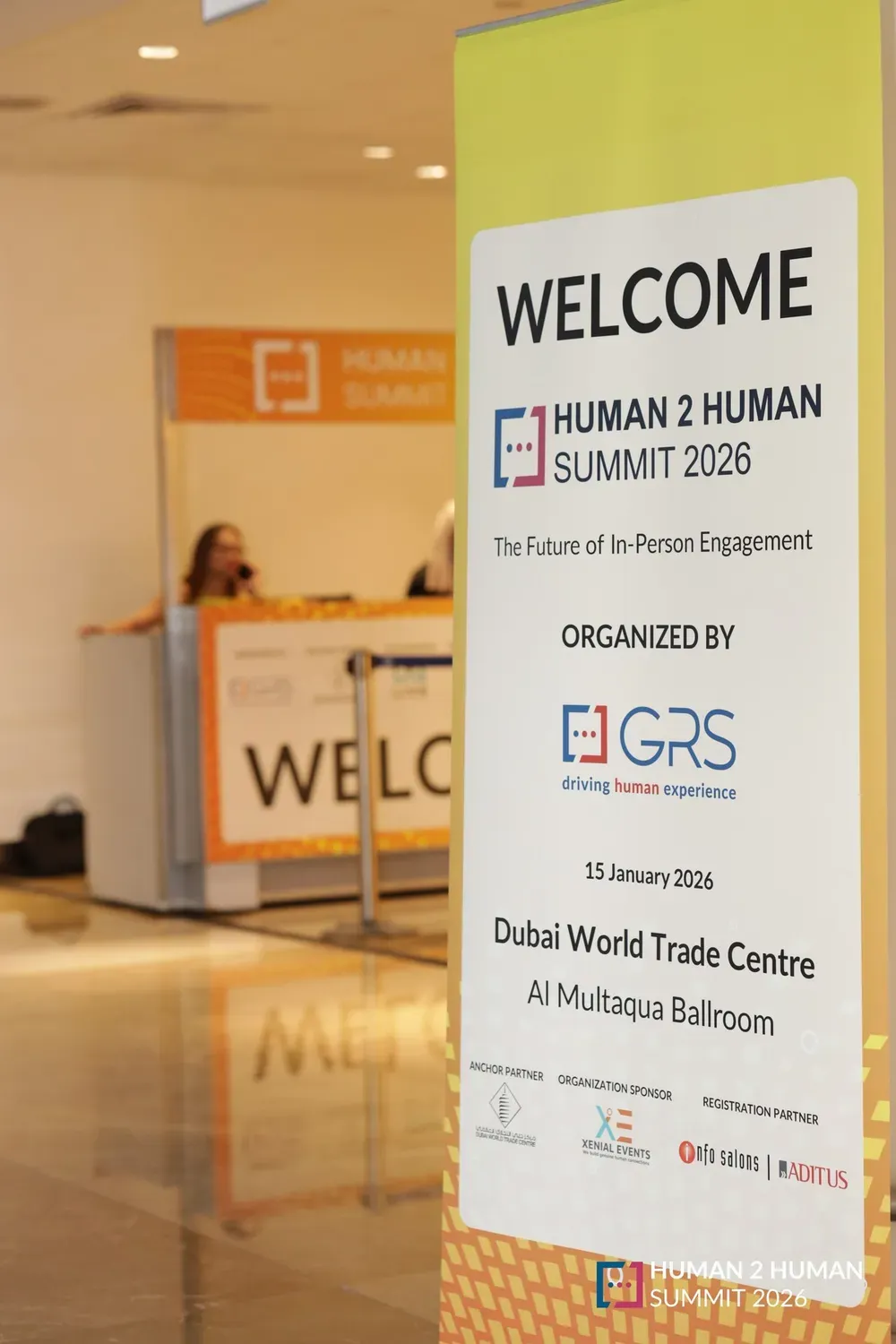 A tall welcome sign at the entrance for the Human 2 Human Summit 2026, The Future of In-Person Engagement, organised by GRS, with the registration desk behind it