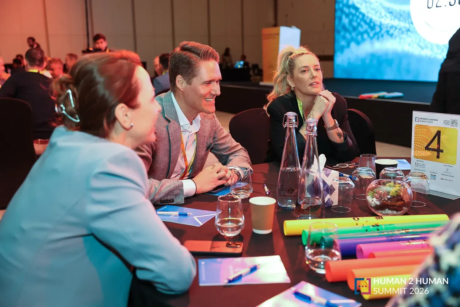 A woman and two men seated at a round table, listening intently during a summit session