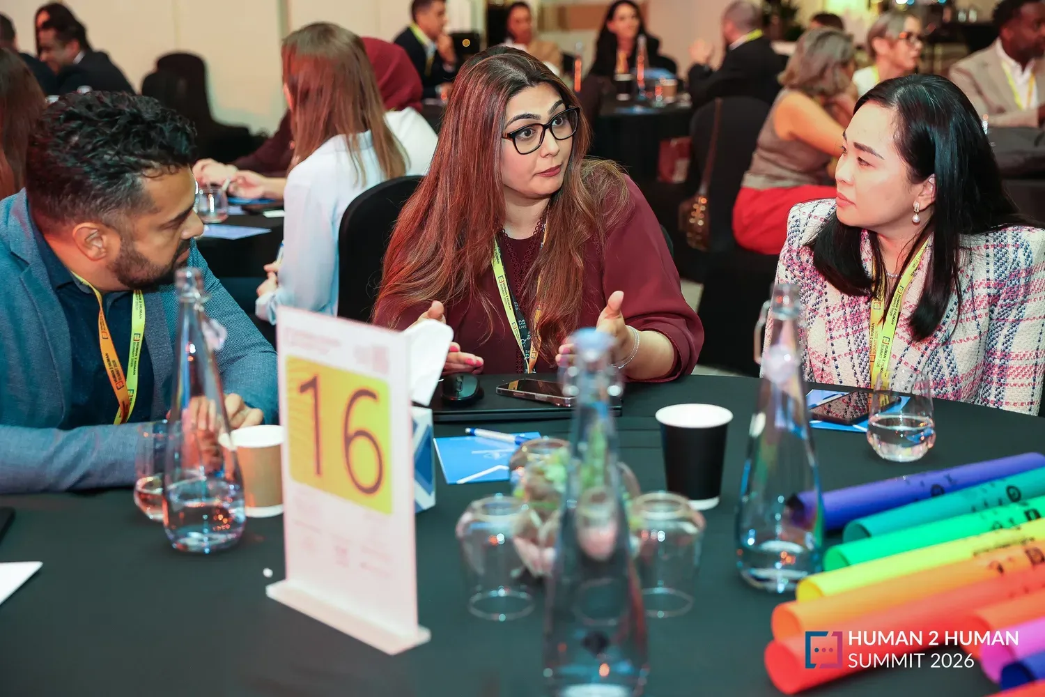 Attendees in discussion at round table 16, a woman in glasses speaking while the people beside her listen