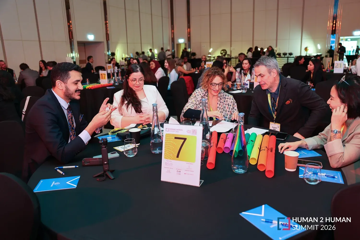Guests leaning in to a round-table discussion at table 7, with colourful percussion tubes on the table in front of them